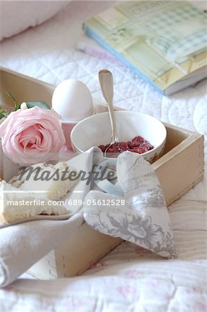 Tray with jam, egg, currant bun and rose on bed