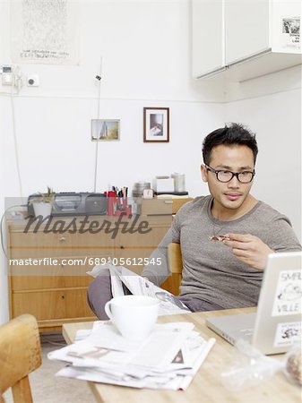 Man with newspaper and laptop having breakfast