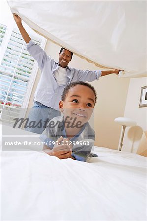 Father holding bed sheet over son (3-6)