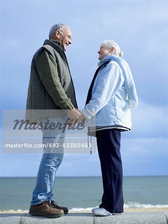 Senior couple standing on wall by water, holding hands