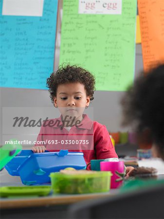 Boy looking into lunch box in classroom