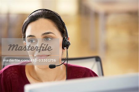 Mid-adult female office worker sitting in cubicle wearing headset, portrait