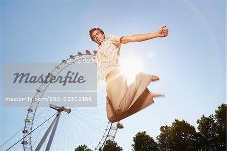 Young man in park jumping in front of London Eye, portrait, low angle view