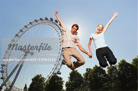 Young couple in park jumping in air in front of London Eye, portrait, low angle view