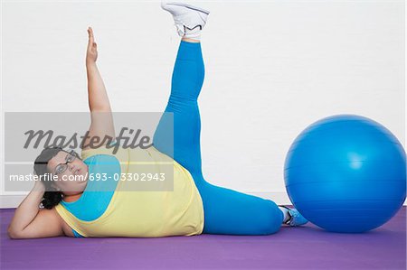 Overweight Woman lying by exercise ball stretching arm and leg upwards -  Stock Photo - Masterfile - Premium Royalty-Free, Code: 693-03302943