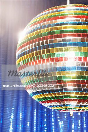 Multi-coloured disco ball in front of blue stage curtain, cropped