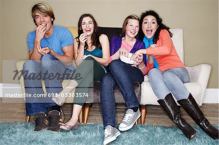 Friends sitting, eating popcorn, watching movie on sofa