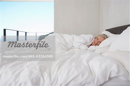 Mature woman lying in bed, smiling