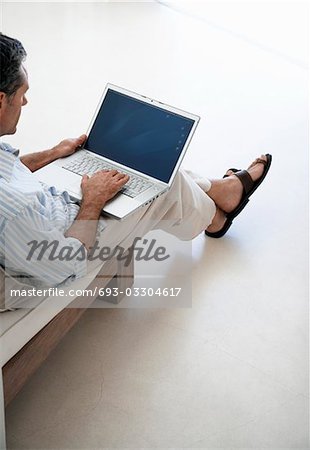 Man using laptop, sitting on sofa in living room, elevated view