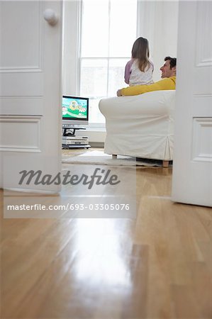 Father and daughter (5-6) watching cartoons in television, back view