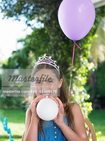 Portrait of young girl (10-12) wearing tiara, blowing up balloons