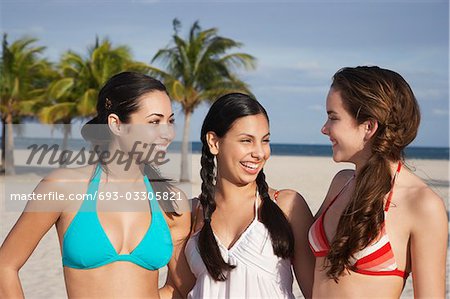Three teenage girls (16-17) wearing bikinis, standing on beach