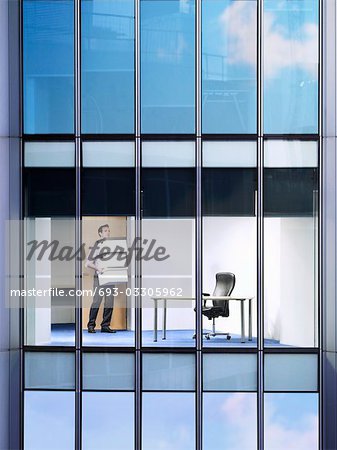 Office worker carrying boxes in office, view from building exterior