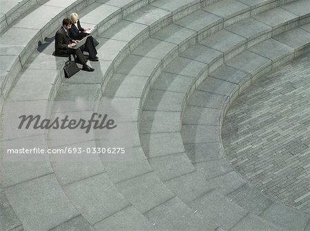 Business man and woman sitting on spiral stairs, using laptop, elevated view