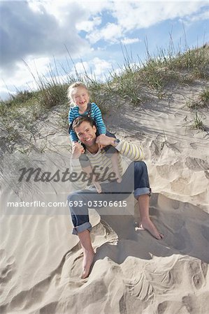 Girl (5-6) sitting on father's shoulders on beach, portrait