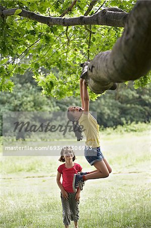 Girl watching friend (7-9) hanging from tree