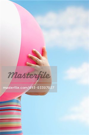 Girl (7-9 years) holding beach ball in front of face, close up
