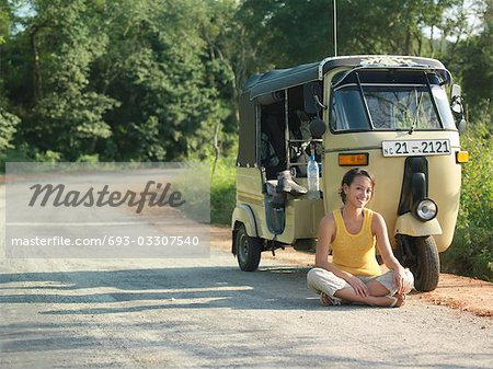 Portrait of young woman sitting cross-legged on road by moto scooter