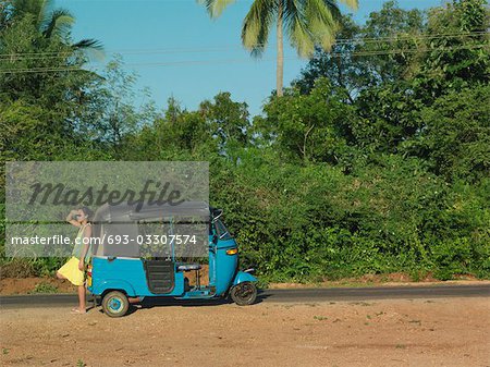 Young woman on dirt road, leaning on old fashioned motor scooter, side view