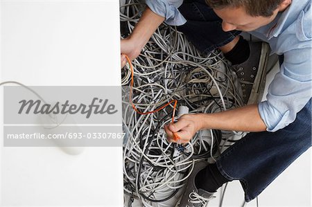 Man working on tangle of computer wires in office