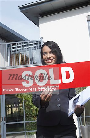 Real estate agent holding sold sign outside house, portrait