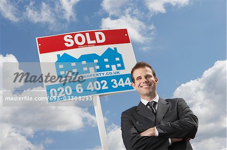 Real estate agent in front of sold sign, against cloudy sky