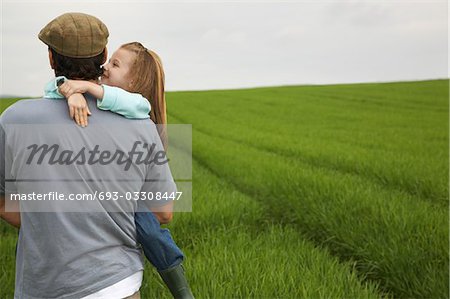 Father embracing daughter (5-6) in field