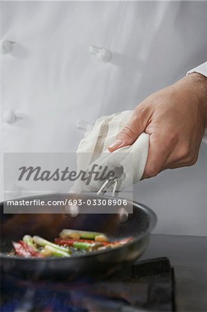 Chef cooking food in frying pan, close-up