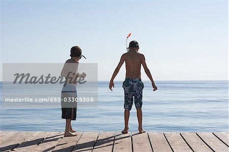 Two boys (7-11) on jetty wearing snorkelling masks, back view