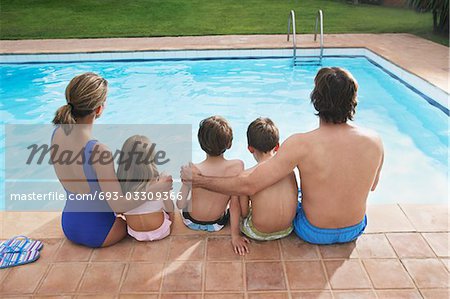 Family with three children (6-11) sitting by pool, back view