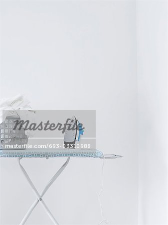 Iron and laundry basket on ironing board against white wall