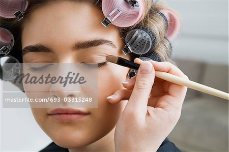 Model in Hair Curlers Having Makeup Applied