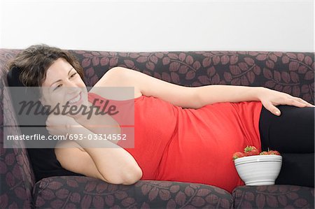 Pregnant woman with bowl of strawberries on sofa