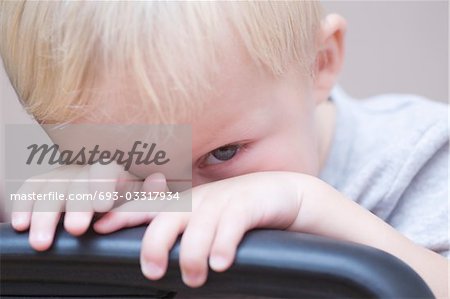 Blonde toddler peeks over chair, looking at camera