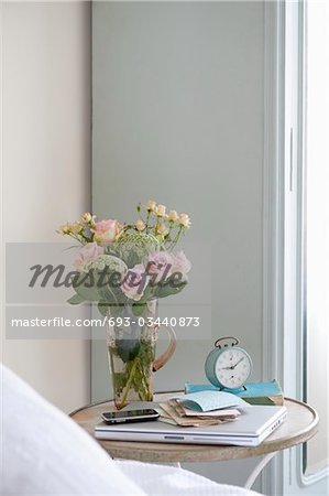 Roses in vase on bedside table with books and alarm clock