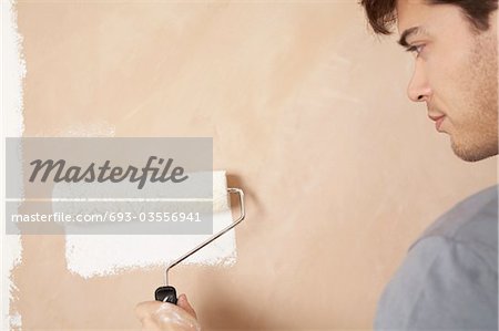 Man painting wall with paint roller, indoors, close up