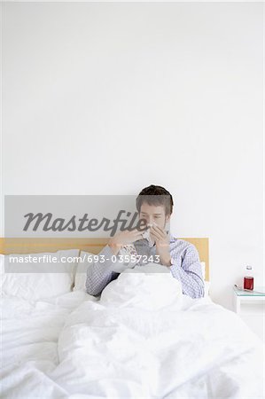 Man with cold in bed blowing nose