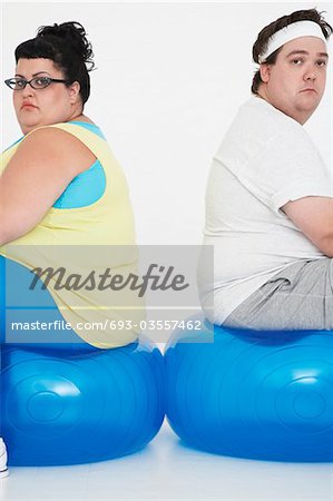 Unhappy overweight man and woman sitting back to back on exercise balls, portrait