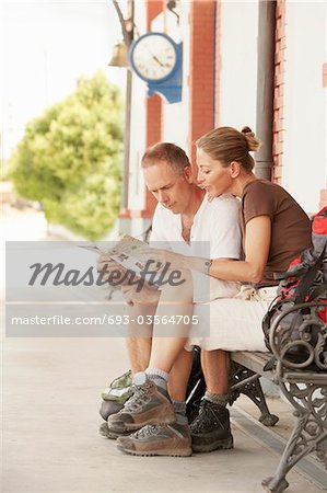 Hiking couple looking at map, sitting on railway platform