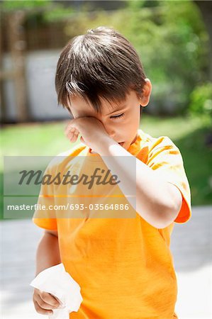 Boy with cold in backyard rubbing eyes