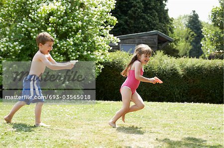 Boy shooting girl with water pistol in back yard