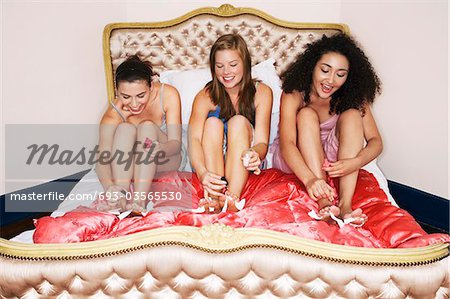 Teenage Girls in pyjamas painting toenails on funky bed at slumber party