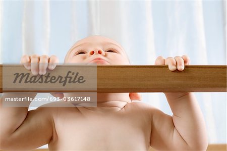 Infant child holding himself up in wooden cot