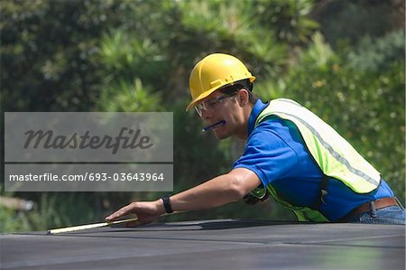 Maintenance worker measures solar array on rooftop, Los Angeles, California