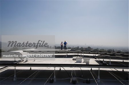 Maintenance workers stand with solar array on rooftop in Los Angeles, California