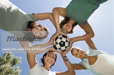Four women holding soccer ball together, view from below.