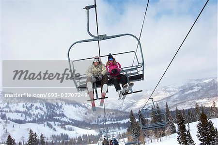 Teenage couple (16-19) wearing skis, sitting on ski lift, low angle view.