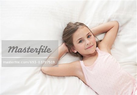 Girl lying down on bed with hands behind head, portrait, view from above