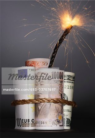 Rolls of money symbolizing dynamite with lit fuse, in studio