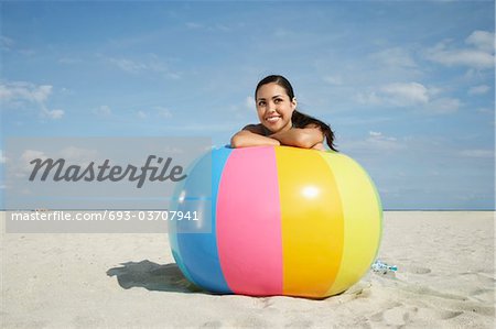 Teenage girl (16-17) sitting behind beach ball on beach, portrait